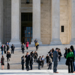 People mill around outside of the classical colonnade and steps of the Supreme Court