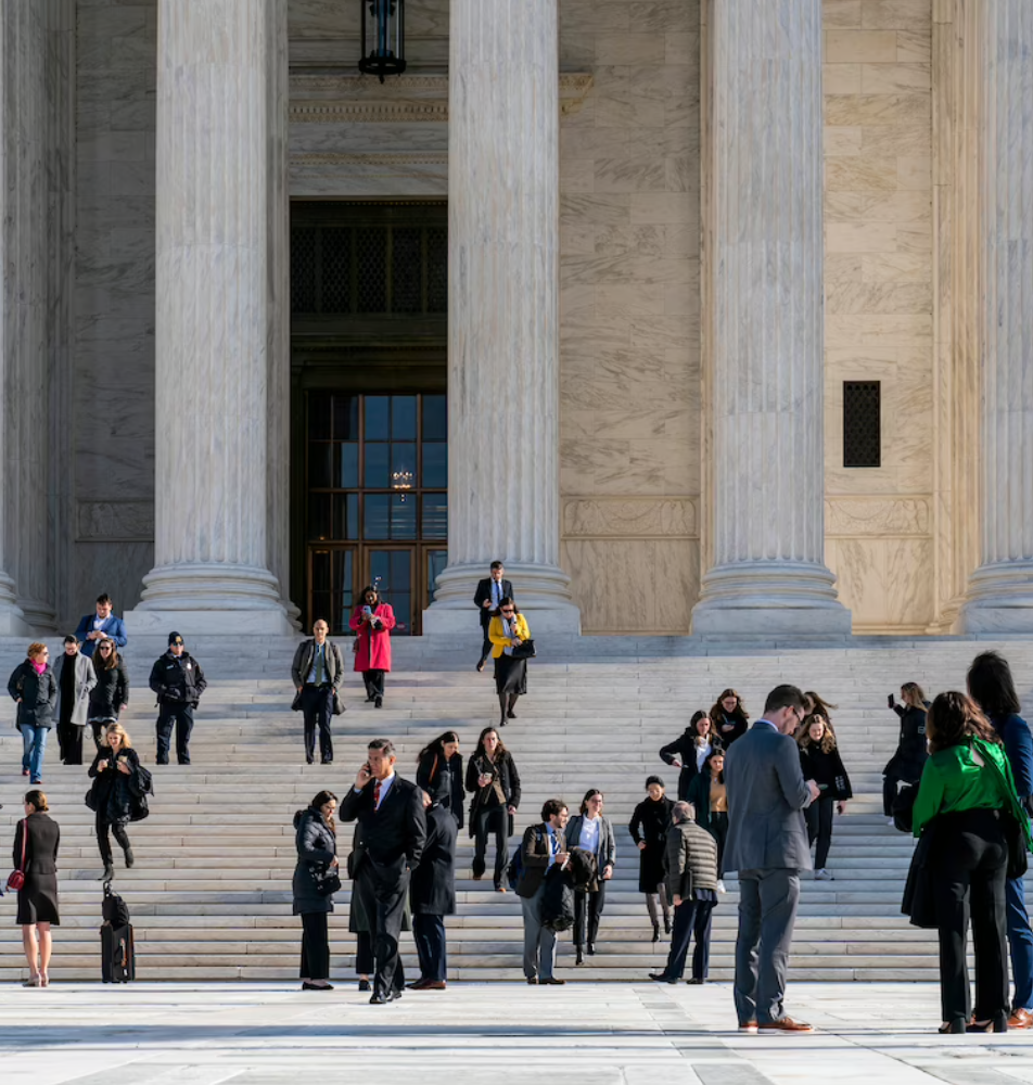 People mill around outside of the classical colonnade and steps of the Supreme Court