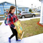Two people carry items into a home