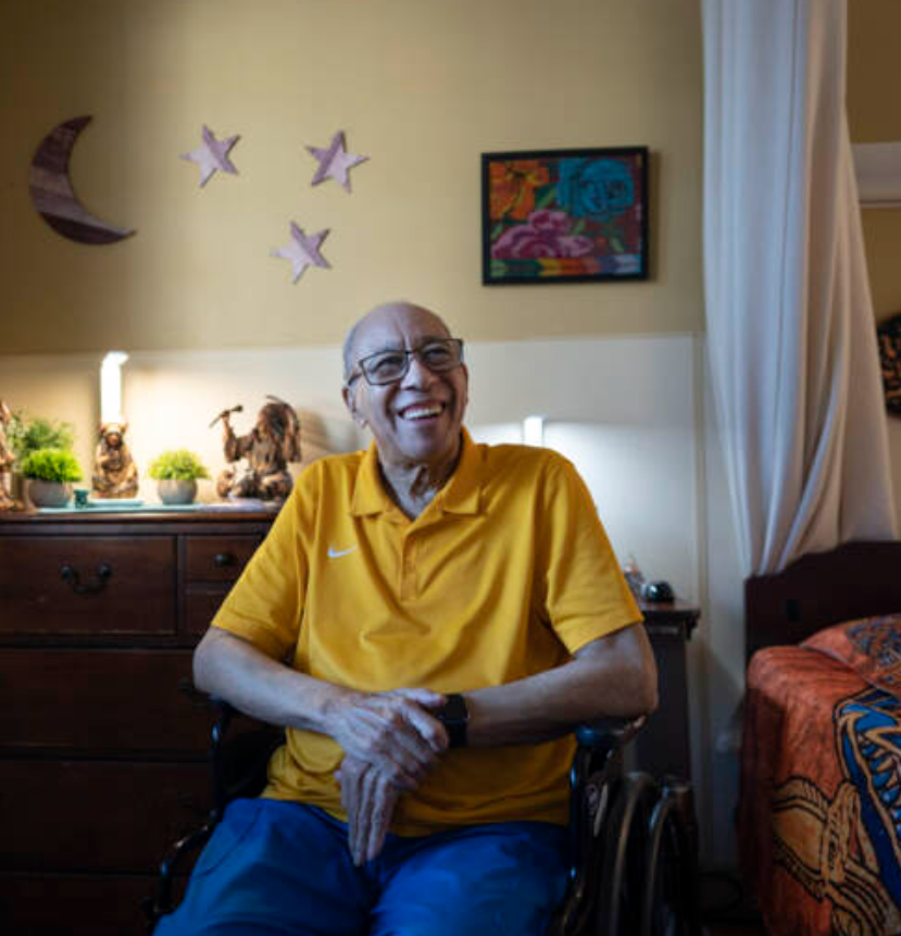 An older person sits in a wheelchair in a bedroom