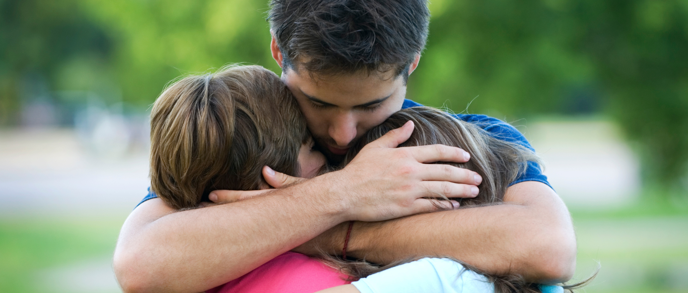 An adult hugs two children close, set outside.