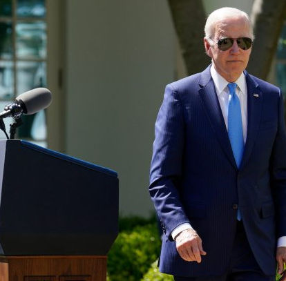 President Biden in his signature aviator sunglasses walks away from a podium outside of the White House
