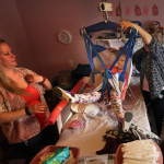 A nurse moves a child to her wheelchair with the help of the child's mother
