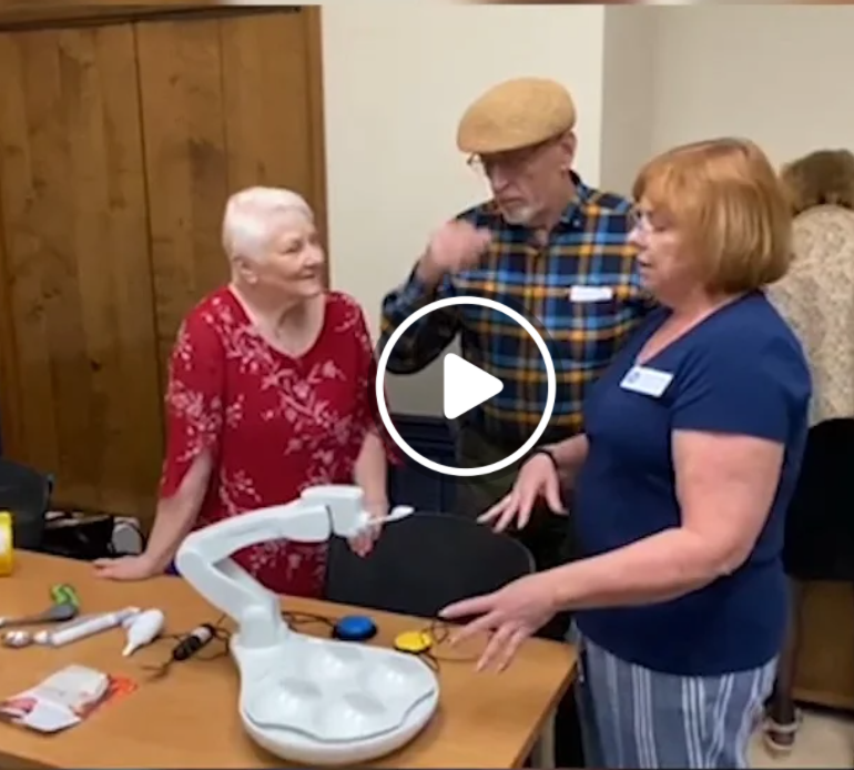 Karen Latimer demonstrates an assistive technology device to an older couple