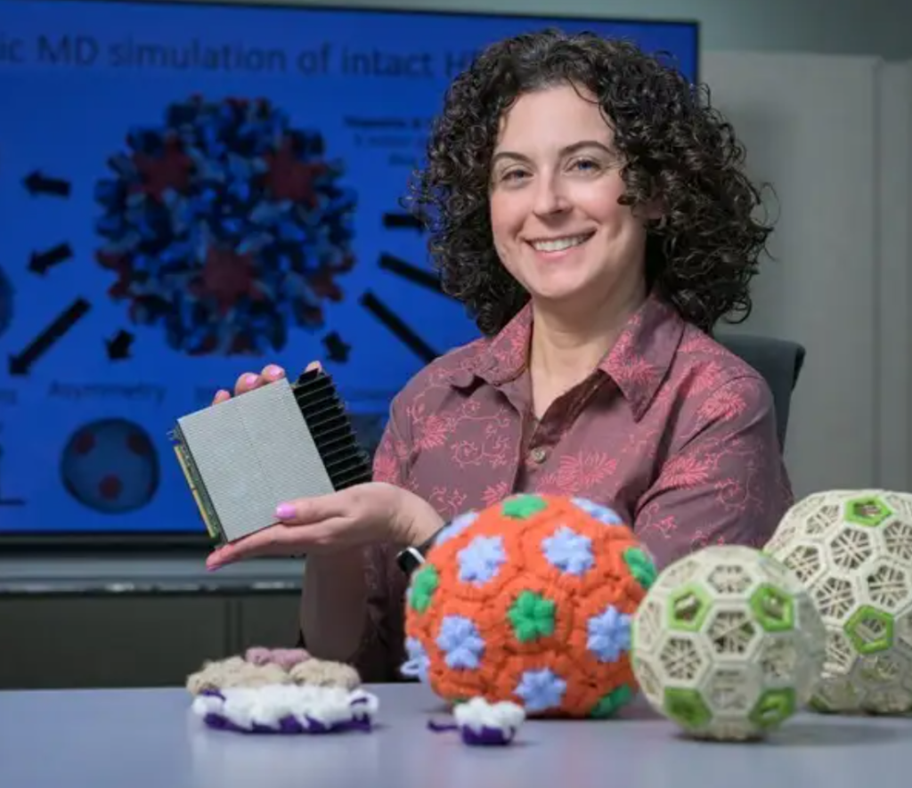 Jodi Hadden-Perilla poses with crochet models of viruses and a piece of computer equipment