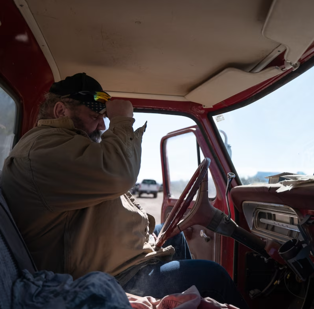 A man in a pickup truck puts on his hat.