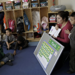 Early education classroom, teacher is reading to the class by a calendar for March.