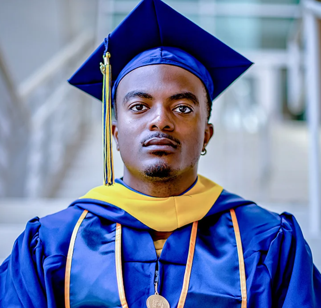 A person with dark toned skin wearing blue and gold academic regalia