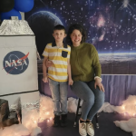 Annie Lloyd with her son Teddy in front of an outer space background with a cardboard spaceship