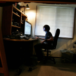 A teen sits at a computer in a dim room.