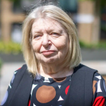 Judy Singer has a shoulder-length light blond bob and wears a boldly printed top and black vest