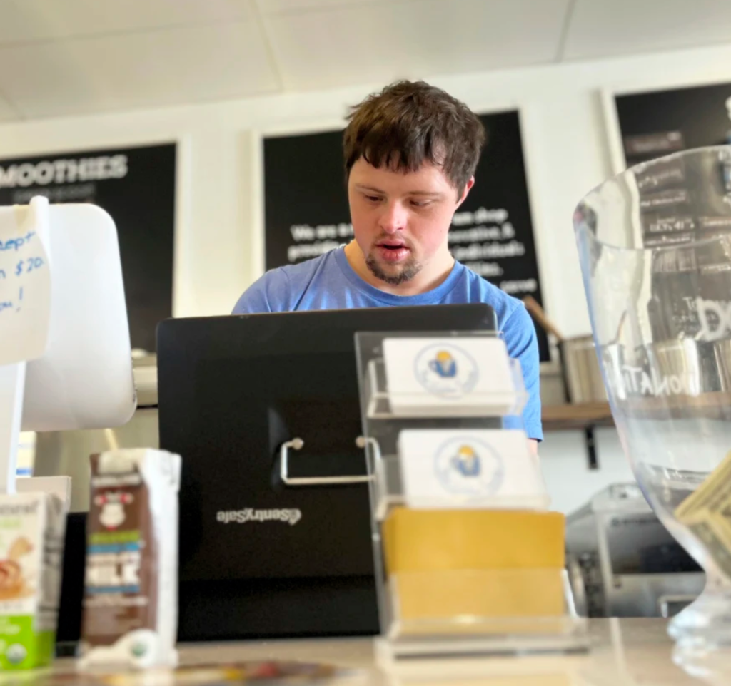 A young adult works a register at a food counter