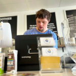 A young adult works a register at a food counter