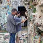 a young adult with an older adult guiding them to touch a wall comprised of heavily textured mosaics