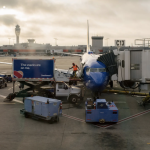 An airplane attached to a jetway being loaded from a truck