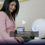 Video still. Dr. Arshia Khan interacts with a small white robot