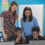 Kelsey Stave and Teresita Cuevas stand by two seated students at the Western Sussex Boys & Girls Club