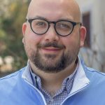 Headshot of Anthony Kokoszka. Anthony is an adult male with glasses and is wearing a light blue, zip-up sweater.