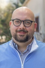 Headshot of Anthony Kokoszka. Anthony is an adult male with glasses and is wearing a light blue, zip-up sweater.