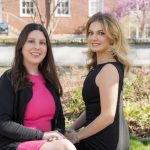 Isabella Haigney has long brown hair and is wearing a pink dress with a black sweater. Grace Mahony has long blonde hair and is wearing a black dress.